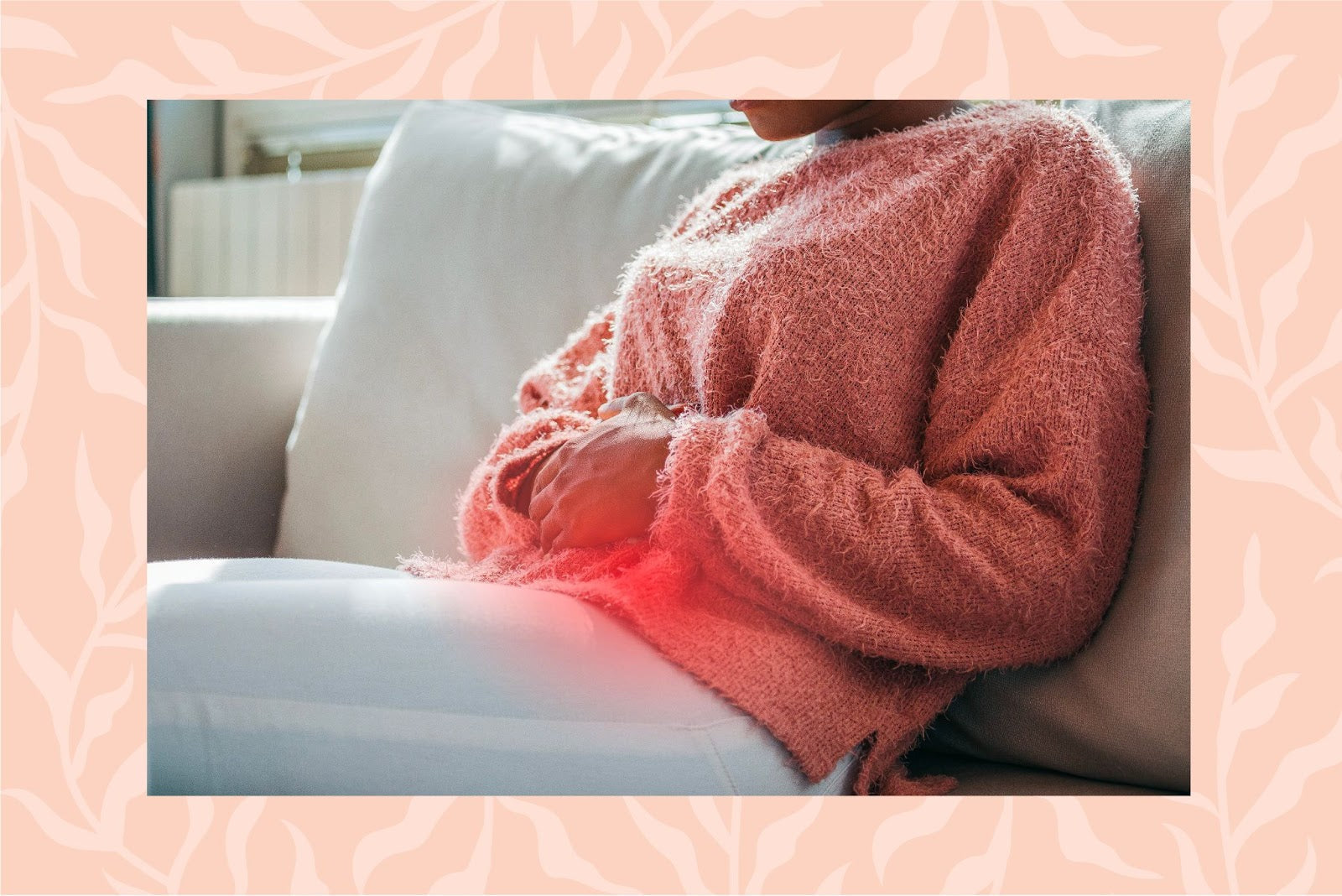 Woman sitting on a white couch holding her gut with the pain area highlighted in red.