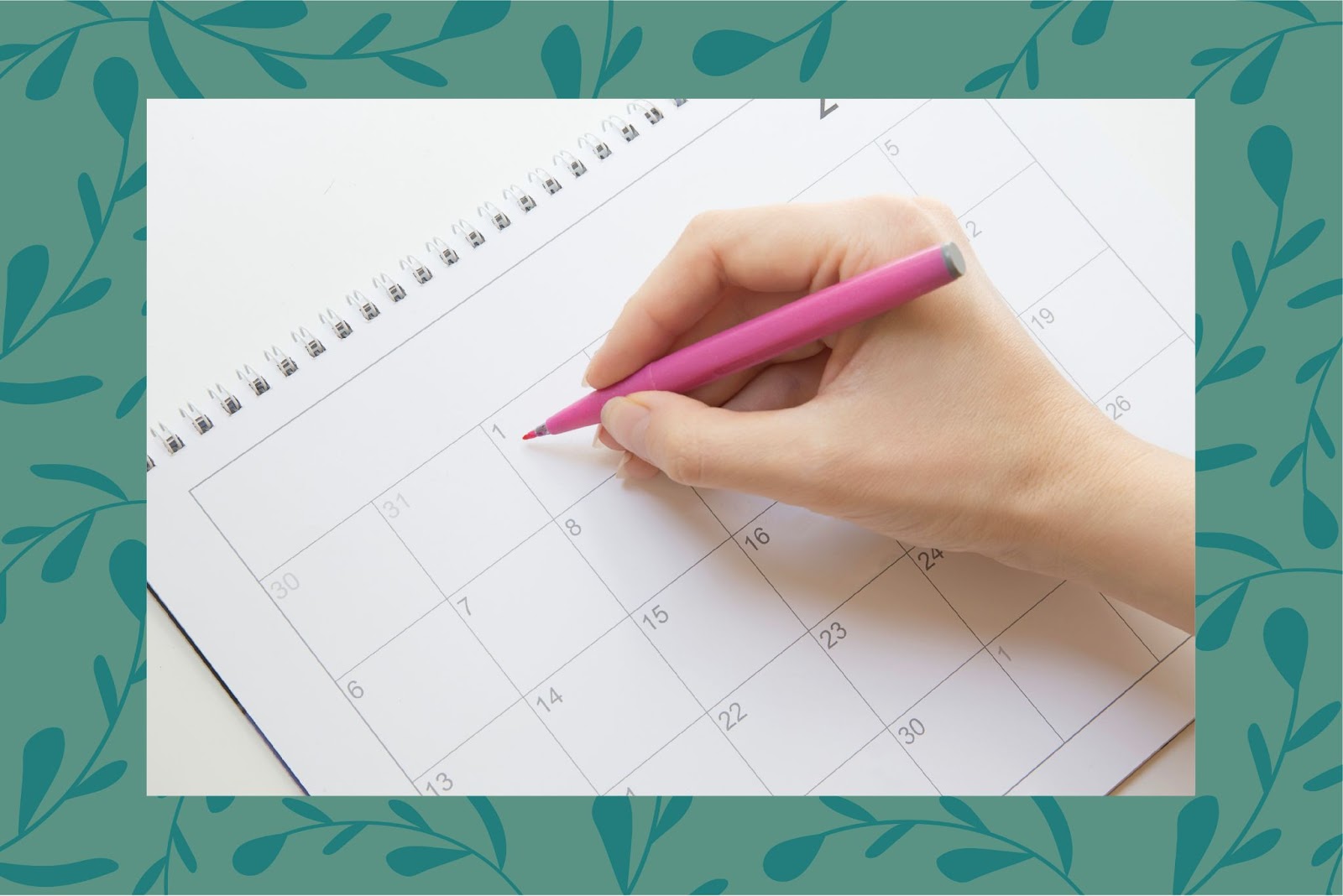 A womans hand holding a pink pen writing on a calendar. 