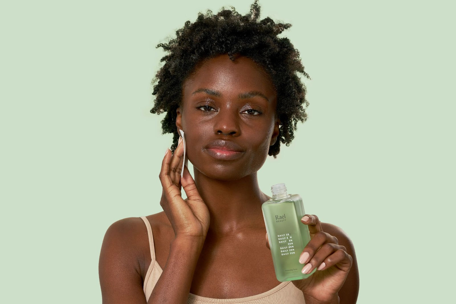 Smiling woman applying skincare products to her face with an applicator pad.