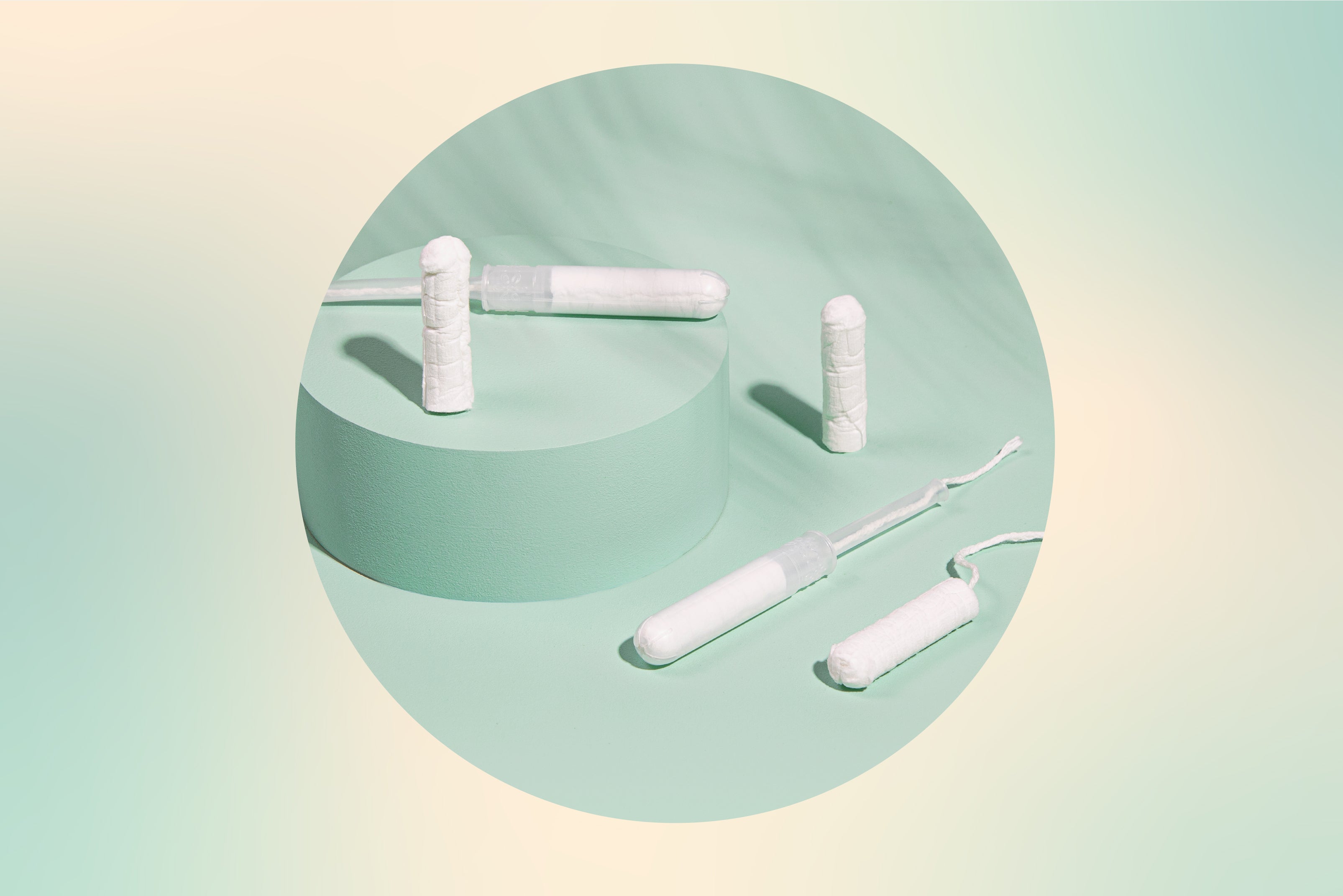 Circle crop image of some unused tampons sitting on a green surface.