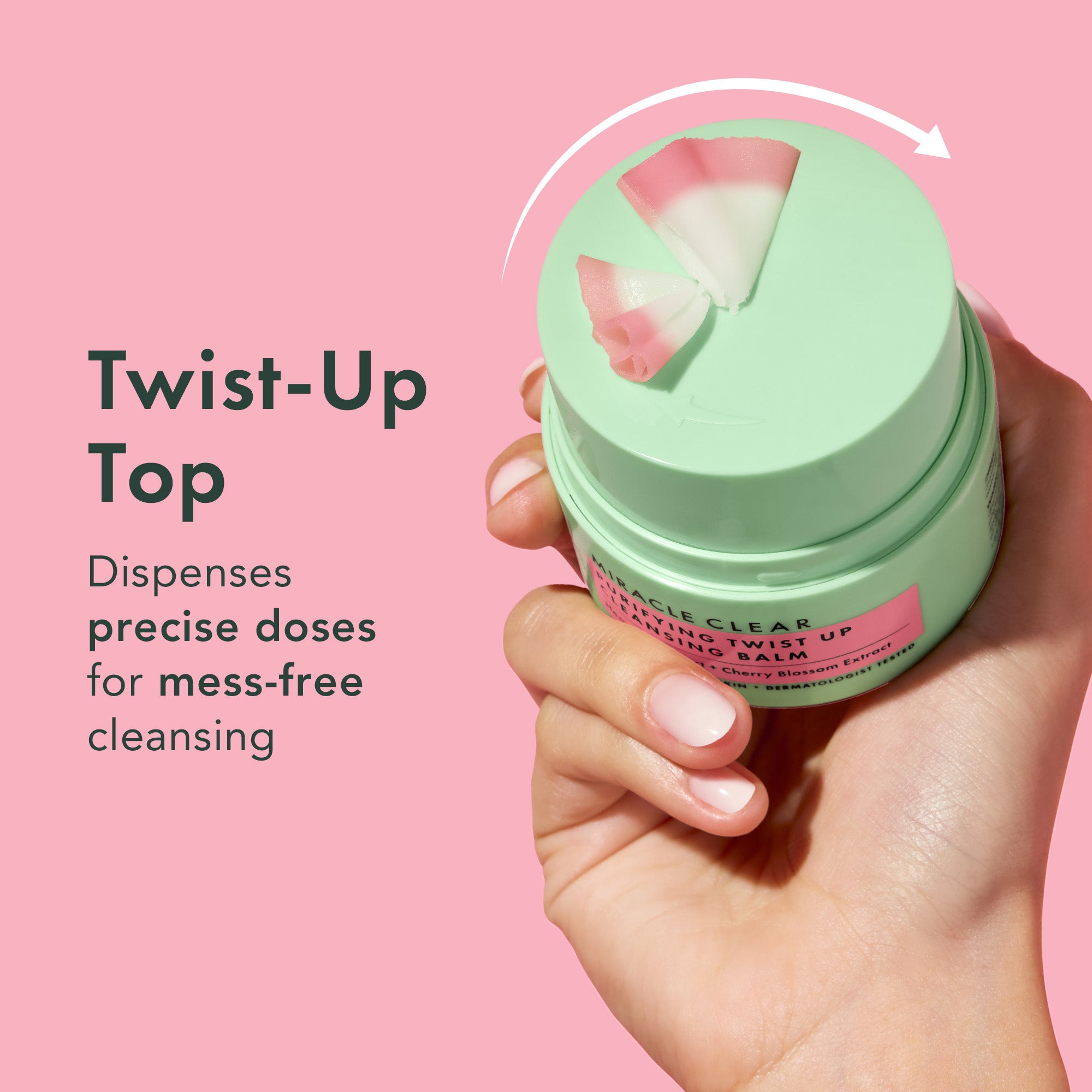 Hand holding a green skincare product with a twist-up top on a pink background