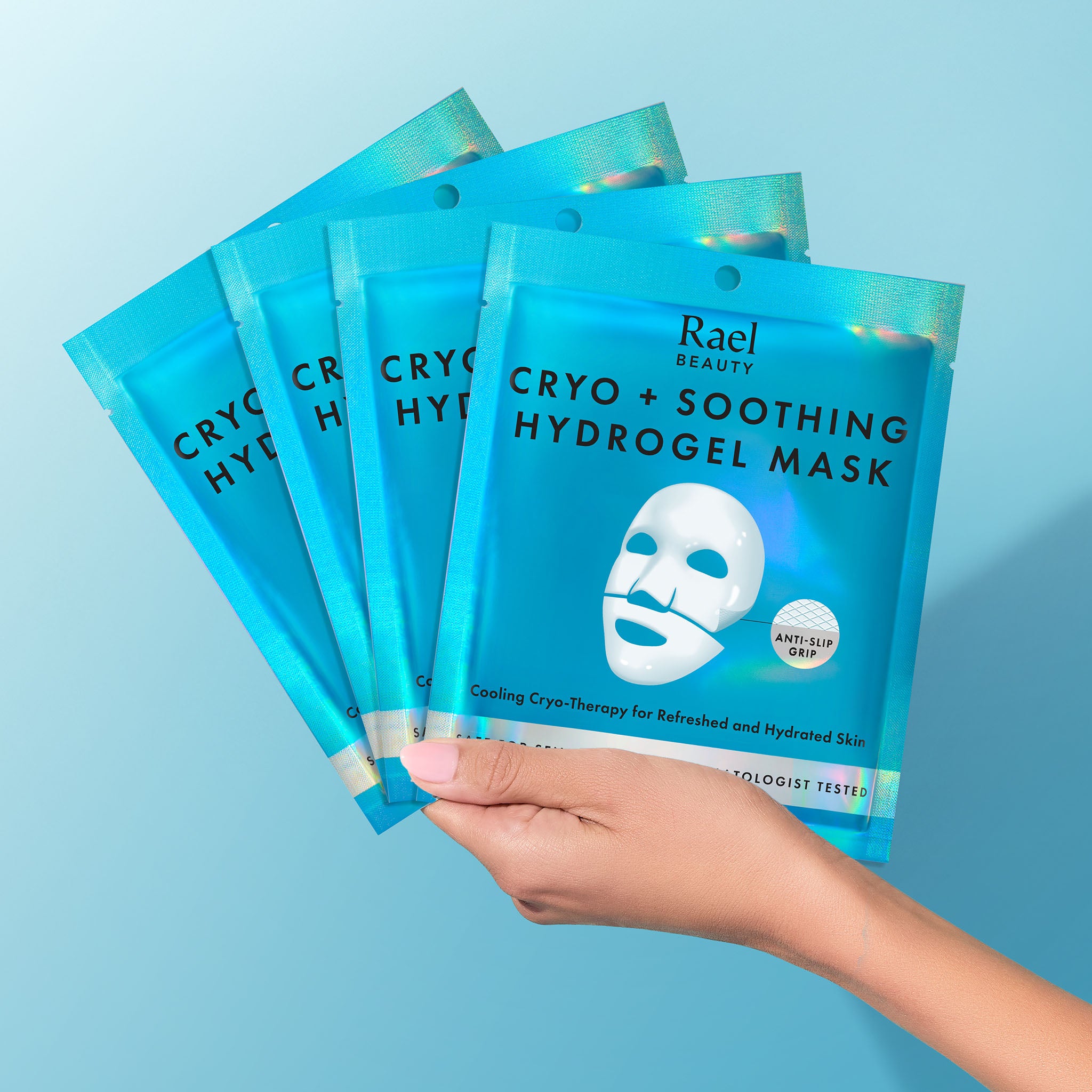 Hand holding Rael Beauty Cryo + Soothing Hydrogel Mask packages against a light blue background