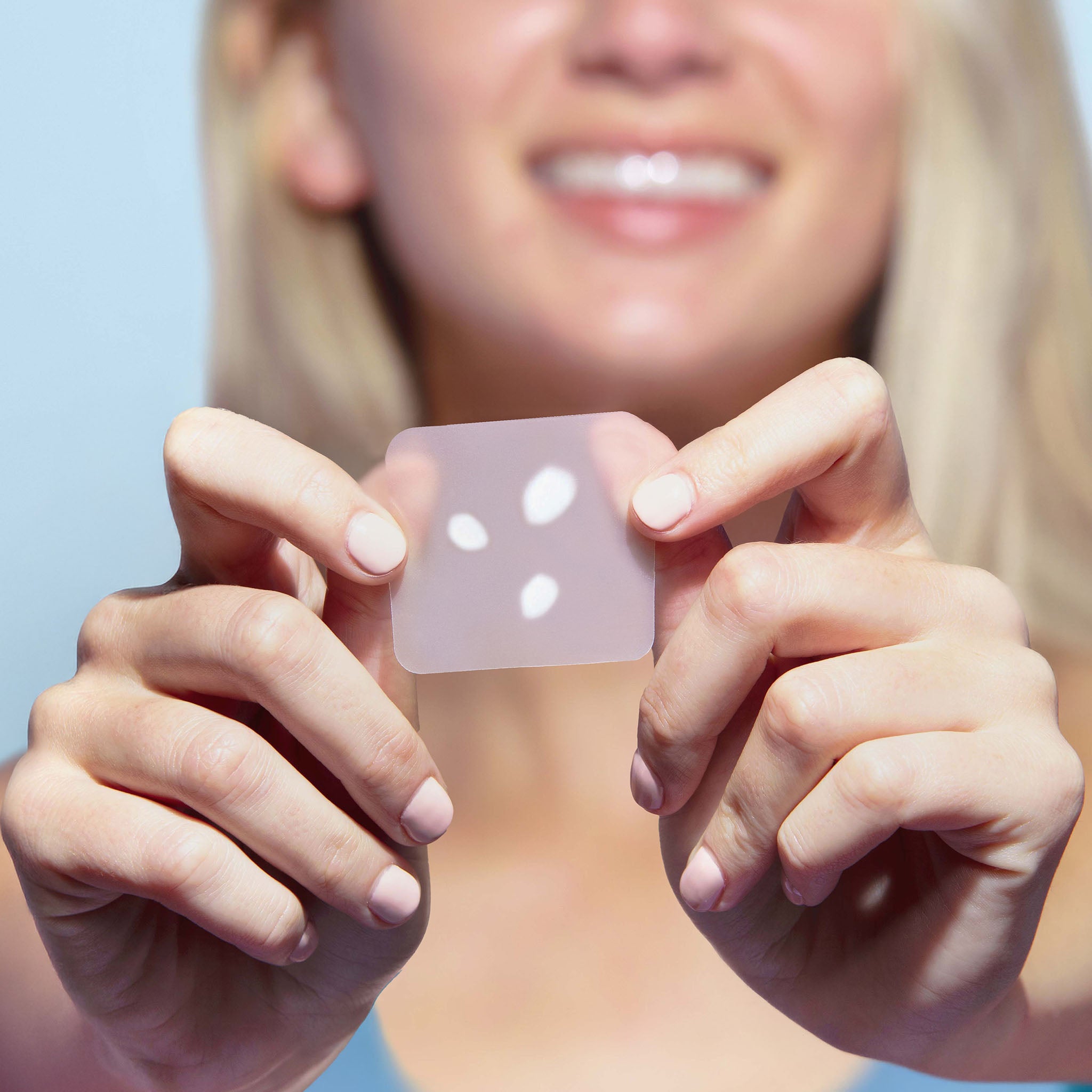 Person holding a clear silicone patch with white dots against a light blue background